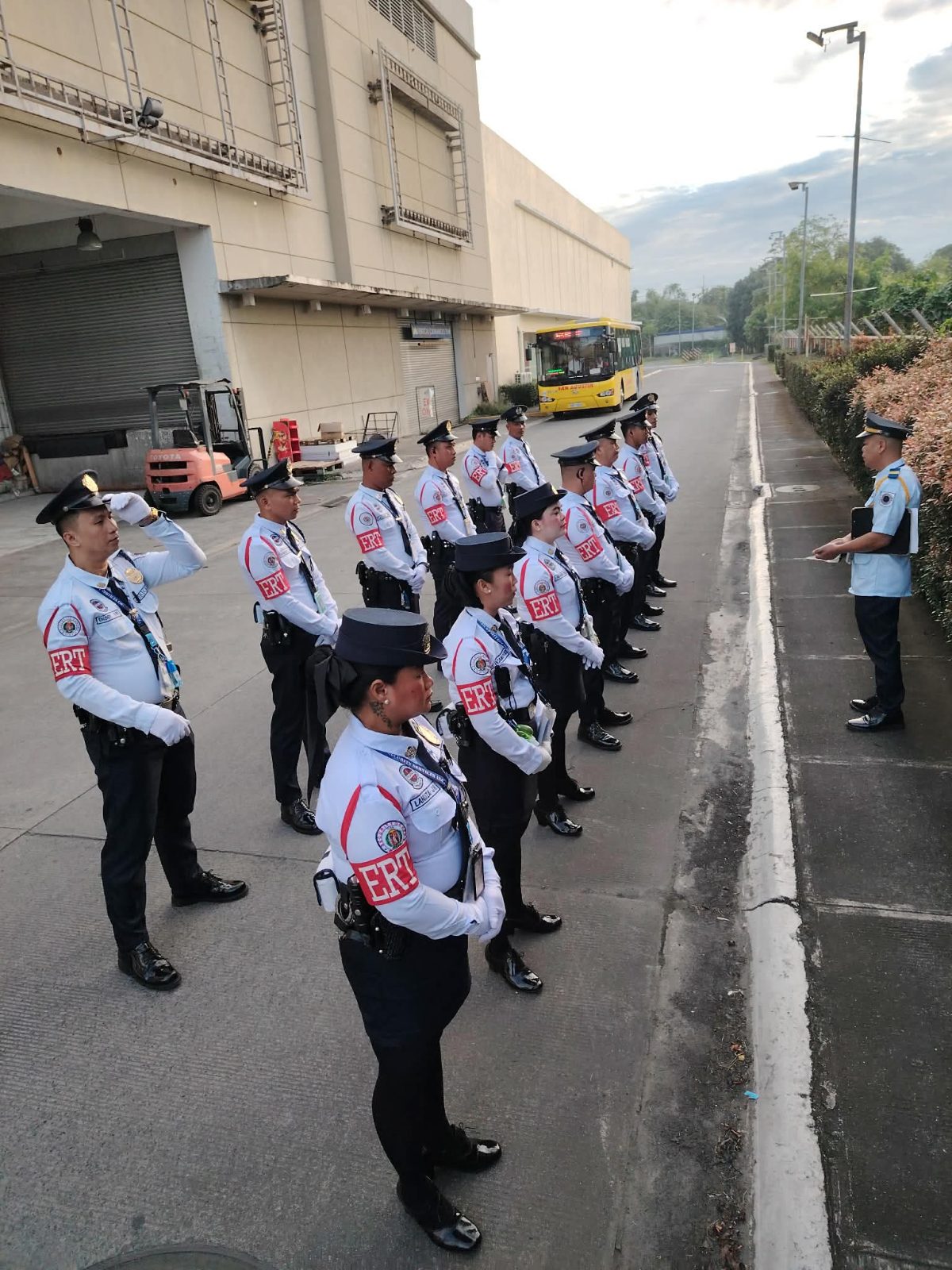 A supervisor briefs a formation of Jericko guards outside a warehouse in daylight
